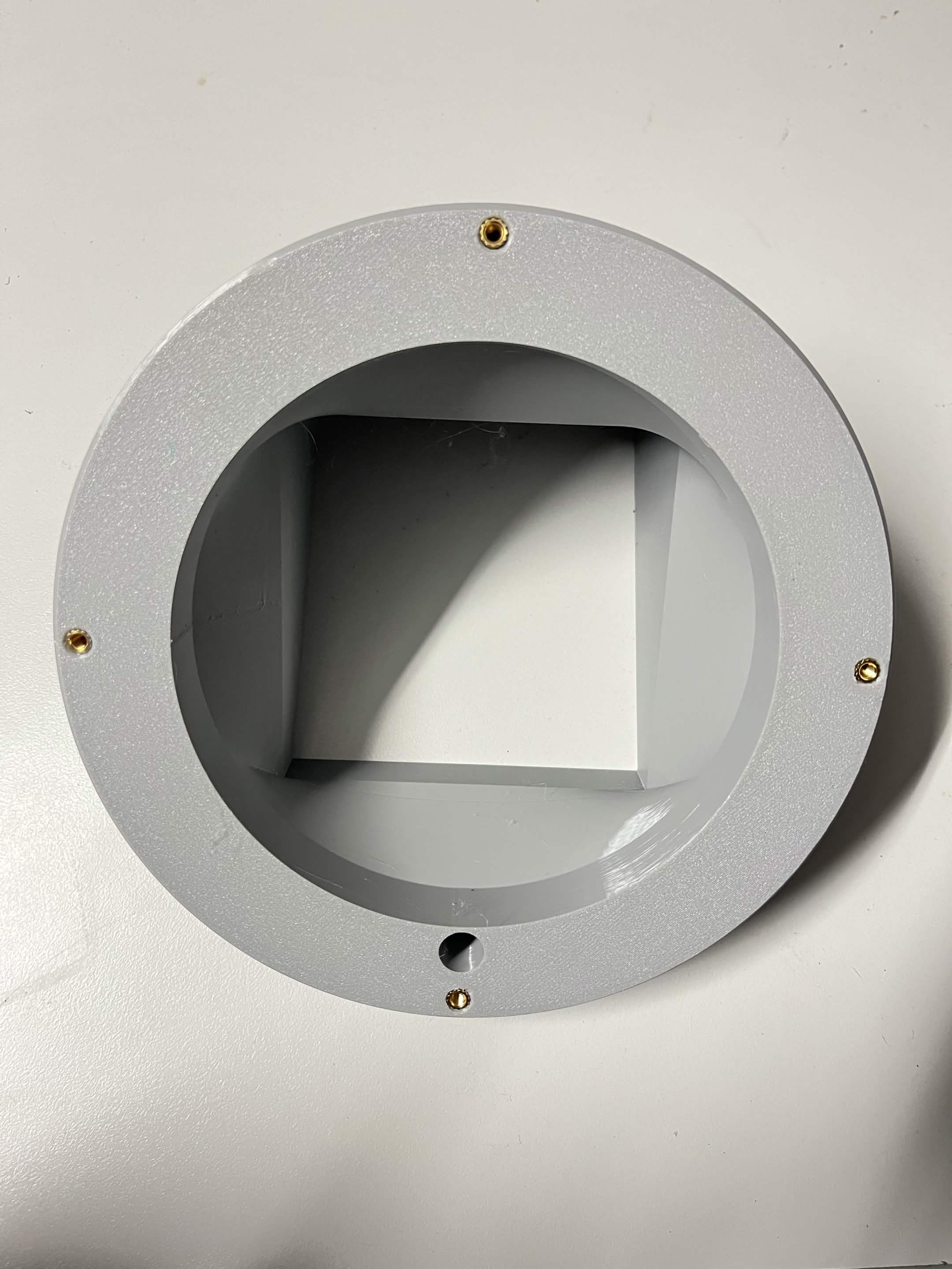 Looking into the Lazy Susan chute mount's circular face: four brass M4 heat inserts around the rim, with the raised square socket for the chute in the middle and the pass-through hole between two of the inserts