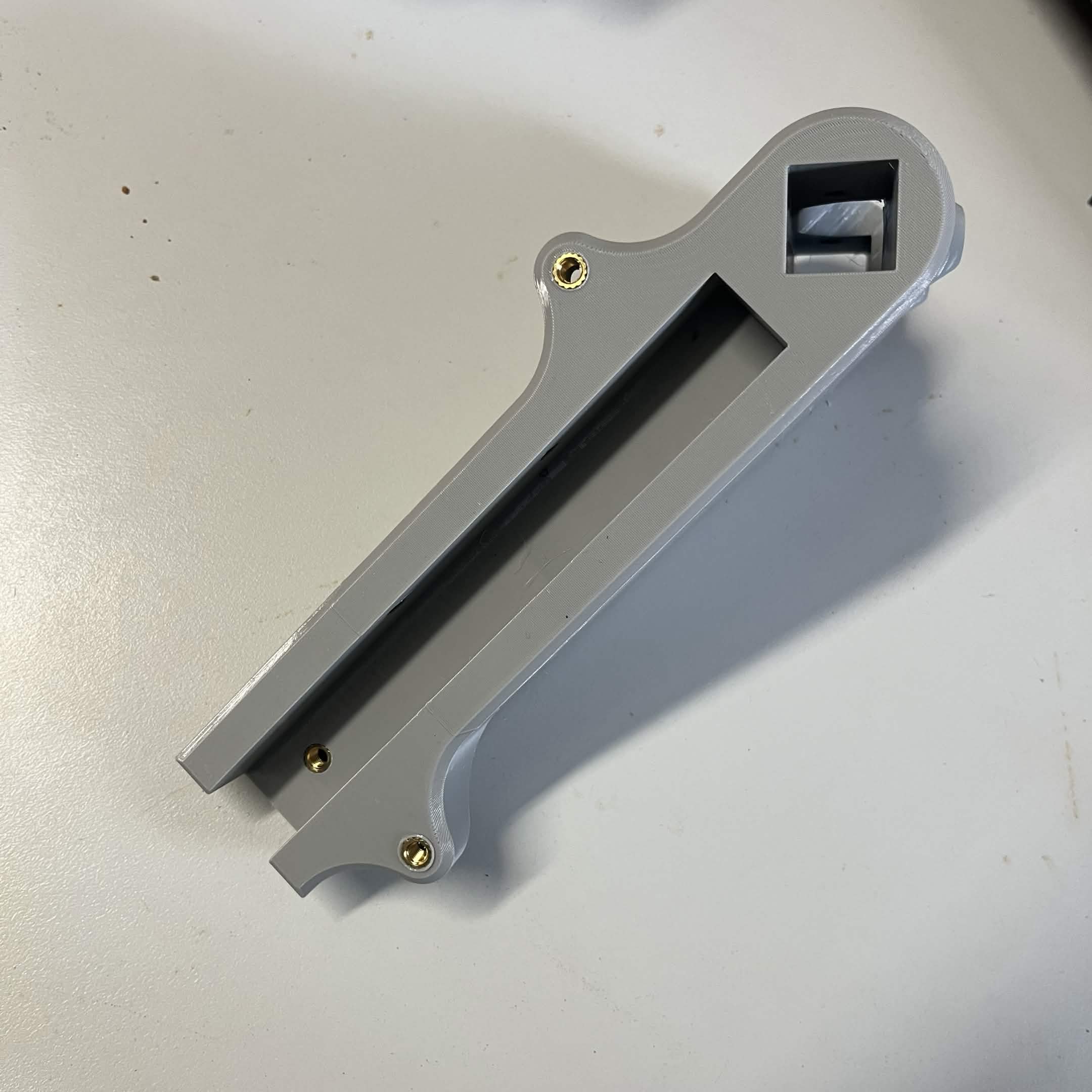 An Interface bracket held up, showing three brass M5 heat inserts: one near the top boss, one in the middle of the channel, and one at the bottom end